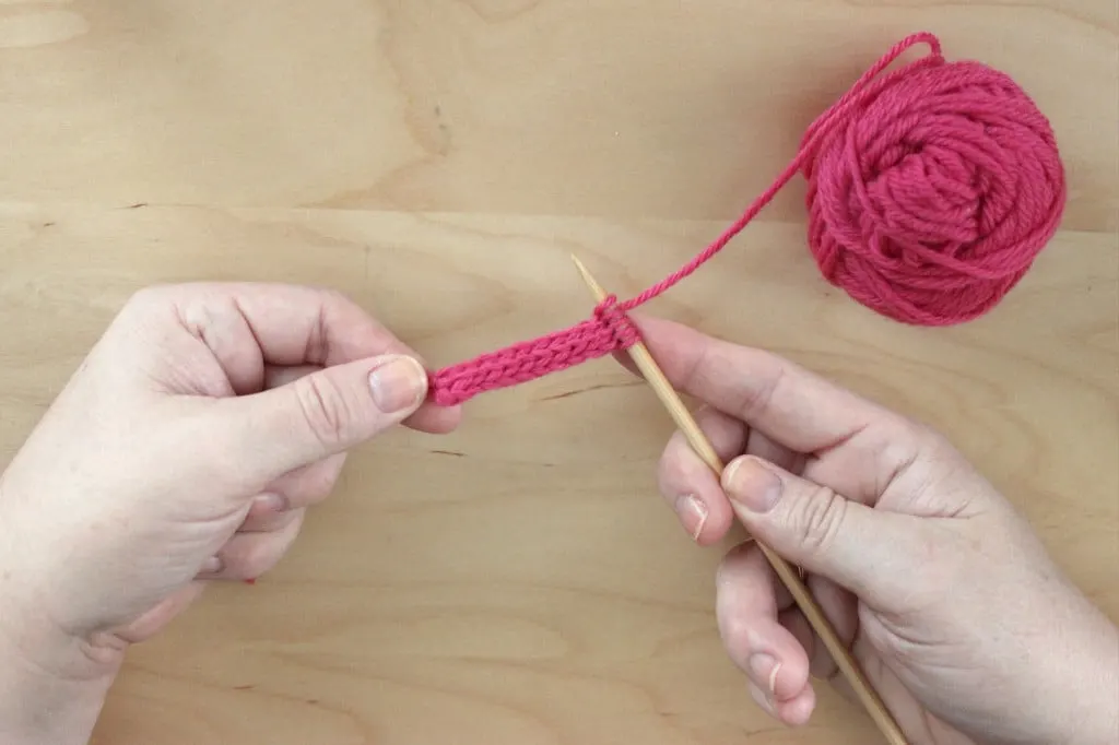 Woman\'s hands holding knitting needles to knit an i-cord with pink yarn.