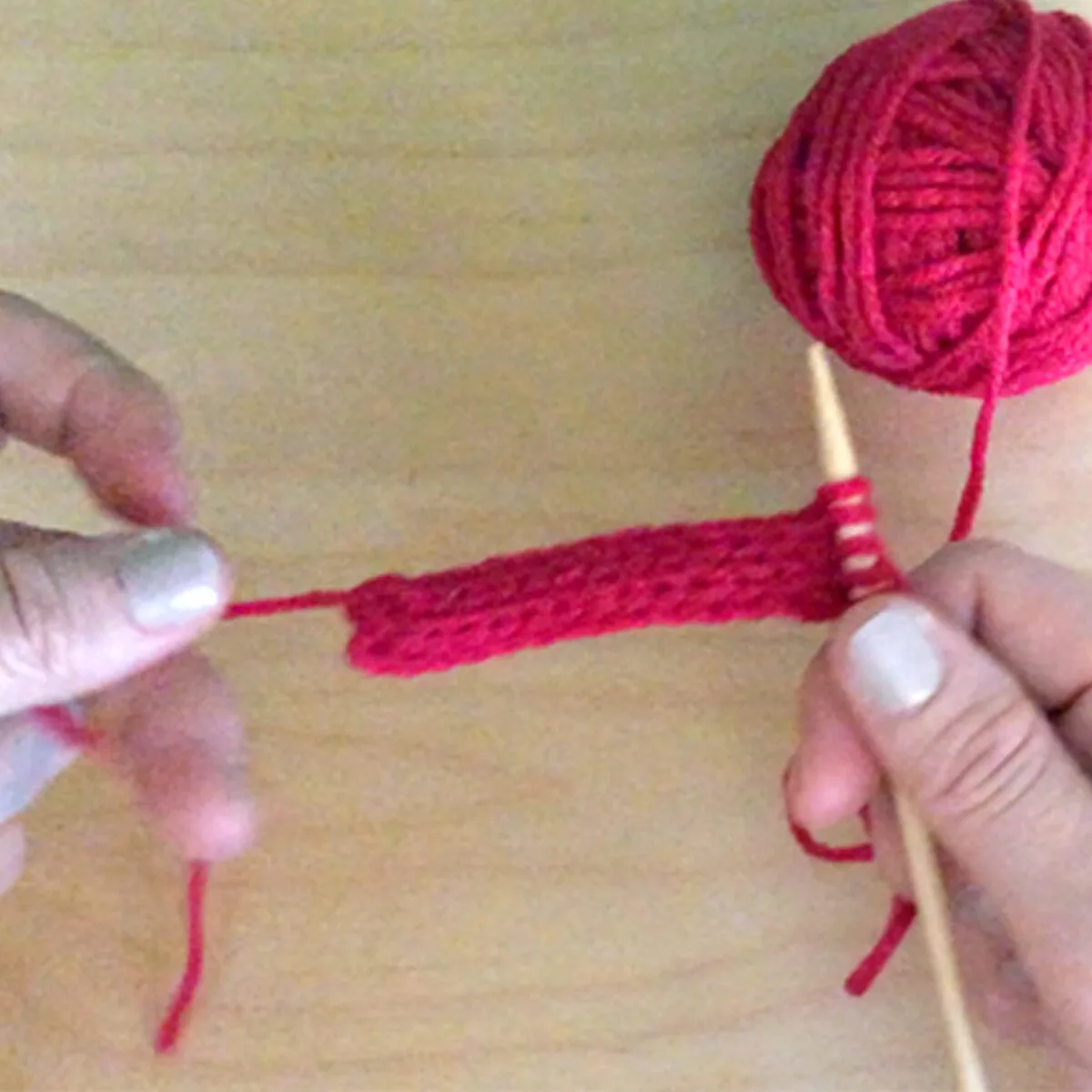 Hands knitting an i-cord with pink yarn and one knitting needle.