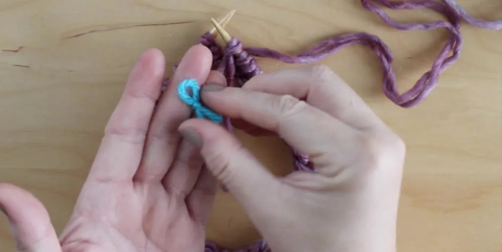 Hands holding blue yarn stitch marker