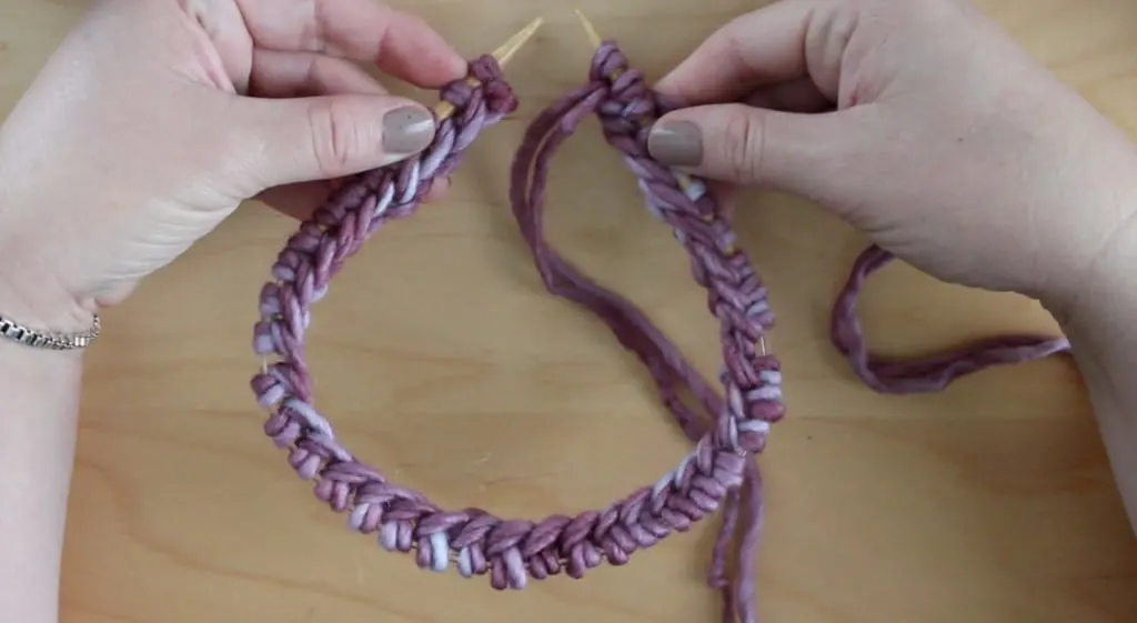 Hands holding a circular knitting needle with purple yarn