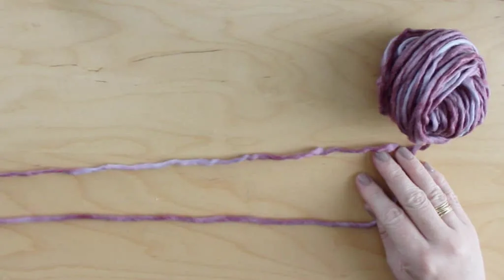 Hands with purple yarn strands on a table