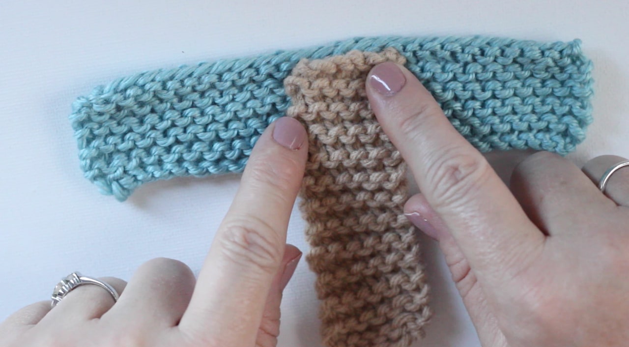 Placing the first swatch of knitting over the second to construct knitted baby booties.