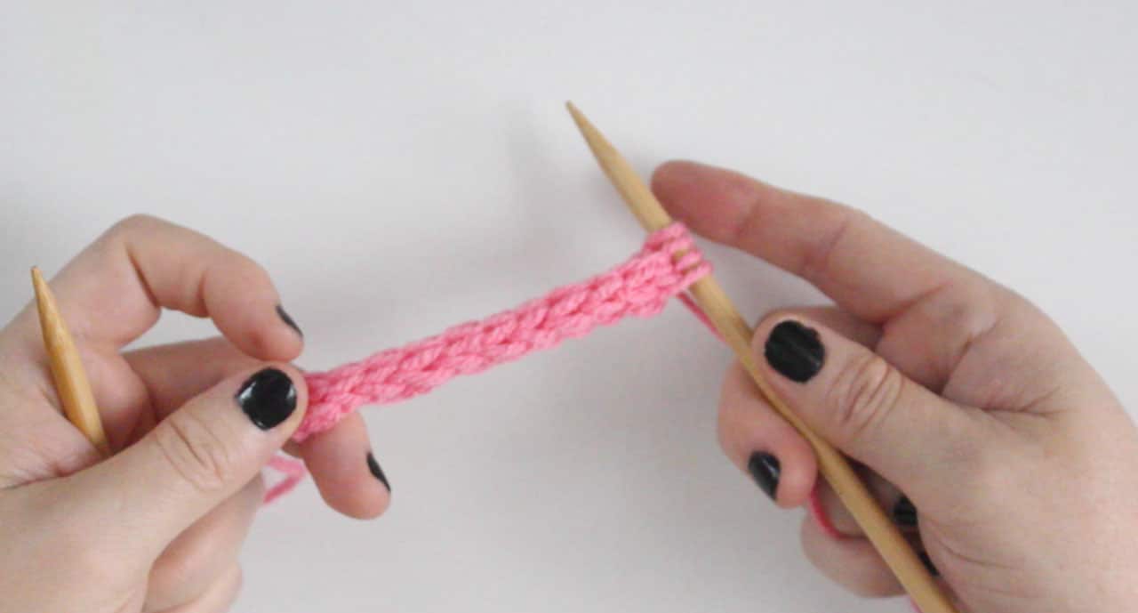 Hands holding a straight knitting needle with knitted icord in pink yarn
