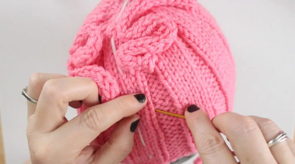 A close-up of hands adding knitted icords onto a Brain Hat in pink yarn