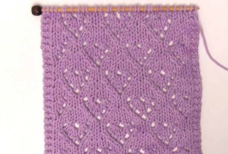 Mini Lace Heart Stitch Knitting Pattern in purple colored yarn on a knitting needle.