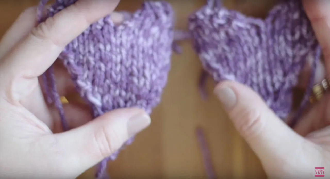 Hands putting two sides of knitted heart together.
