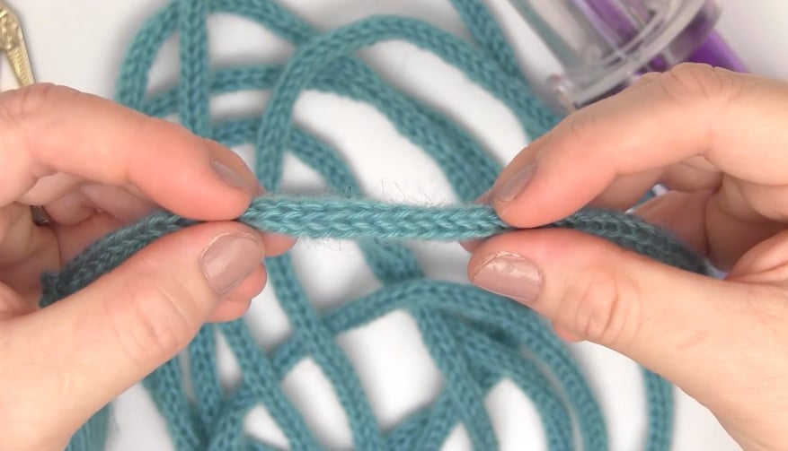 Hands holding a blue knitted i-cord.