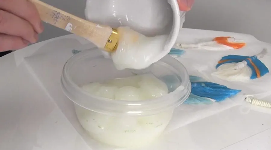 Scooping paste into a container with a paint brush.
