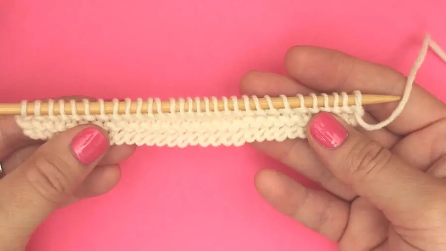 Two hands holding a knitting needle with rows of stitches.
