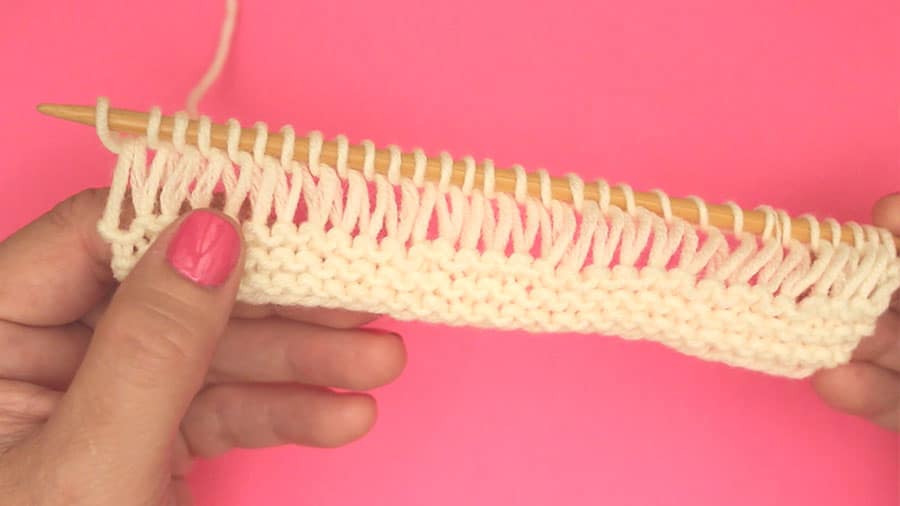 First row of drop stitch garter pattern on knitting needle with white color yarn.