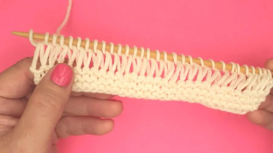 First row of drop stitch garter pattern on knitting needle with white color yarn.