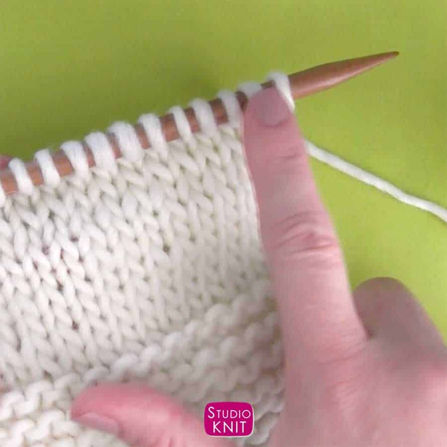 Hand teaching how to knit holding knitted material swatch and knitting needle.
