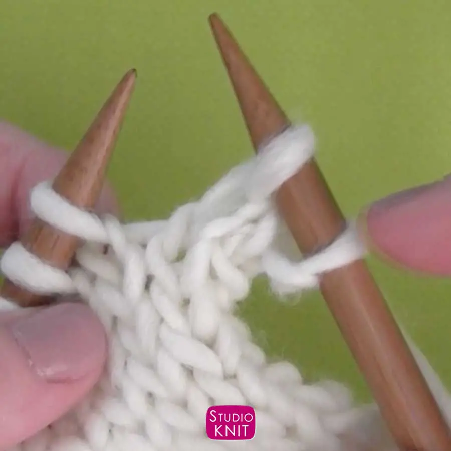knitting stitches in white yarn on straight knitting needles held by hands