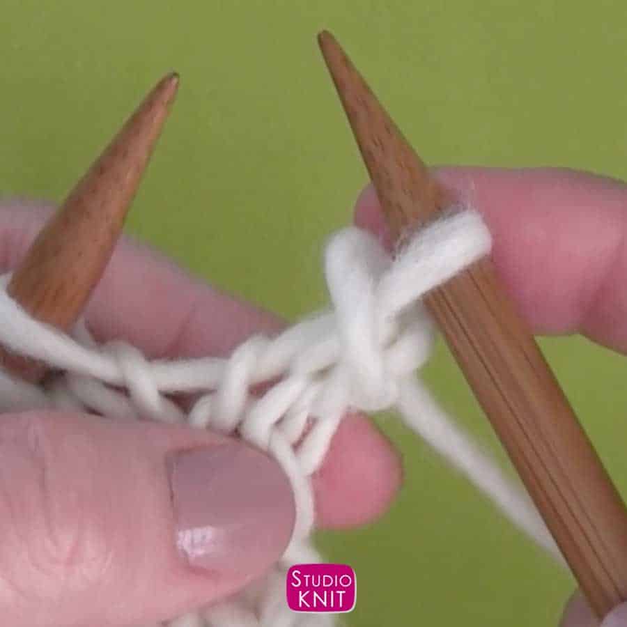 Knitting decrease demonstrated by hands on straight knitting needles with white yarn