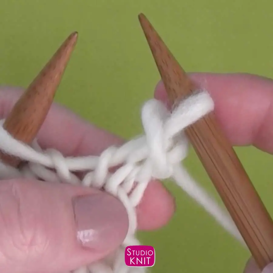 Knitting decrease demonstrated by hands on straight knitting needles with white yarn