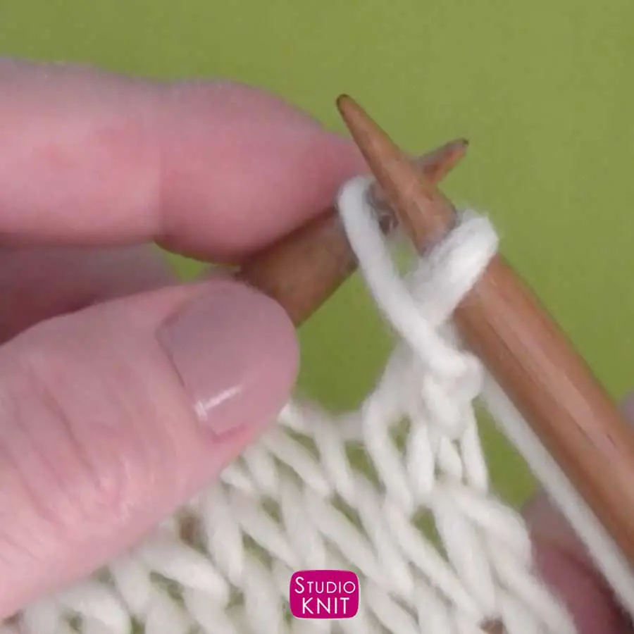 Passing over a knit stitch in white yarn on straight knitting needles held by hands