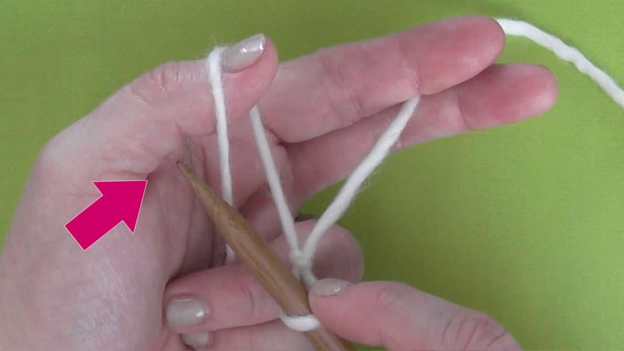 Hands holding yarn in the slingshot method about to cast on stitches onto a straight knitting needle