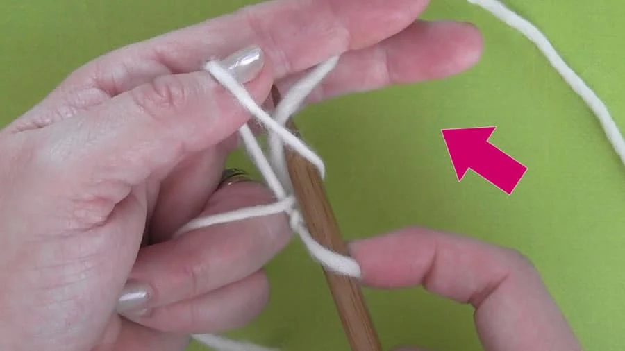 Hands casting on white yarn onto knitting needles 