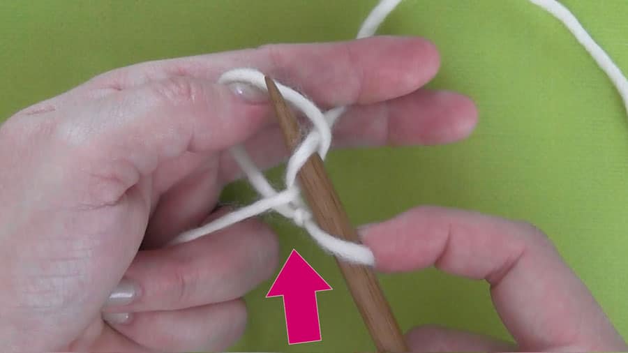 A close up of a hand casting on knitting stitches onto a straight needle
