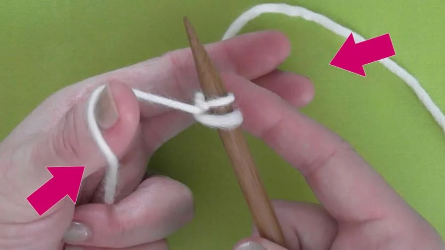 Hands demonstrating casting on knitting stitches with white yarn onto a knitting needle