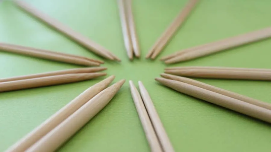 Ten pairs of straight wood bamboo knitting needles arranged in a circle on a green background