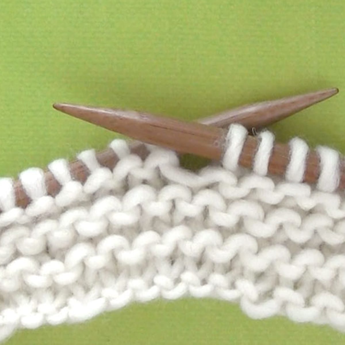 Garter Stitch Knitted Pattern cast on knitting needles in white yarn atop a green background.
