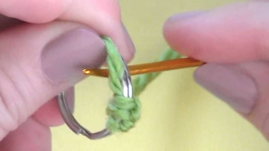 Hands winding yarn around a key ring with tapestry needle.