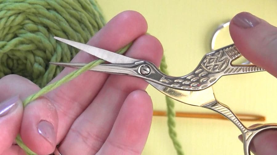 Crane scissors cutting green colored yarn.