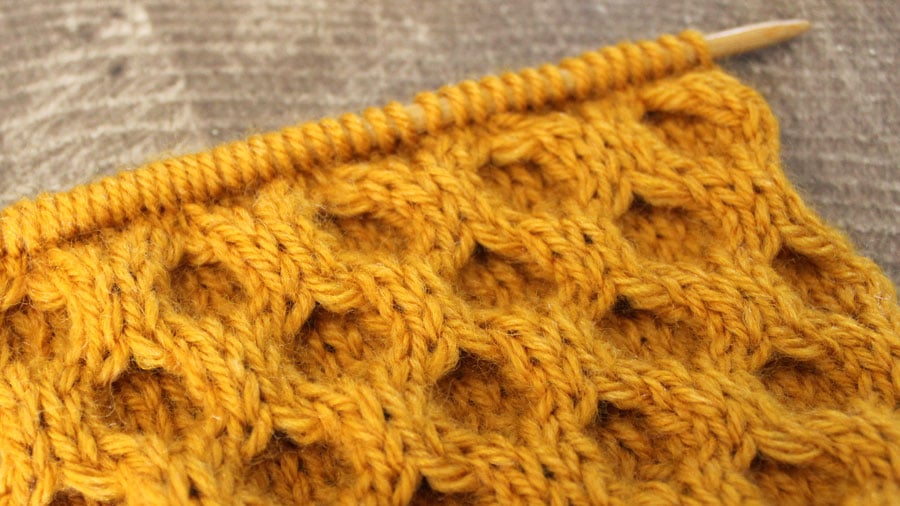 A side view close up of Honeycomb Cable knitted swatch in gold yellow yarn on a straight knitting needle