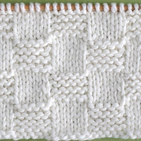 Close up a swatch of textured Garter Checkerboard Stitch in white yarn on a knitting needle