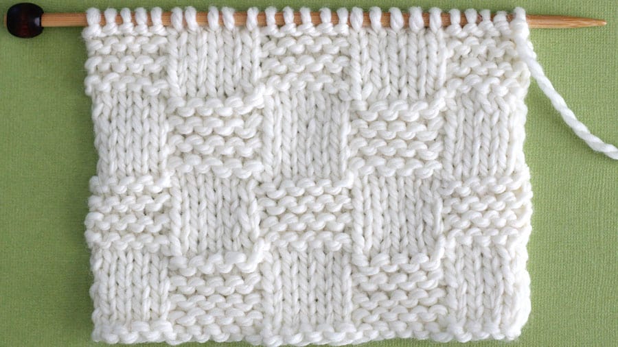 Close up a swatch of textured Garter Checkerboard Stitch in white yarn on a knitting needle