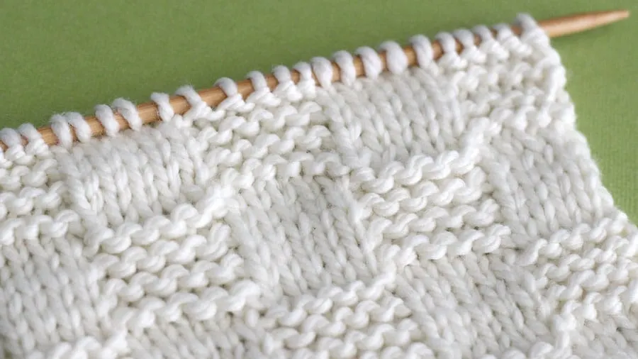 Side view of Close swatch of textured Garter Checkerboard Stitch in white yarn on a knitting needle