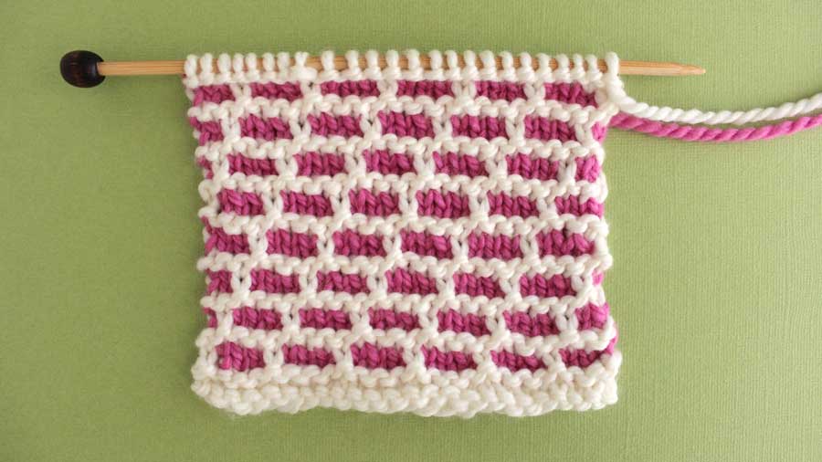 Swatch of the Brick Stitch with pink and white yarn on a knitting needle.