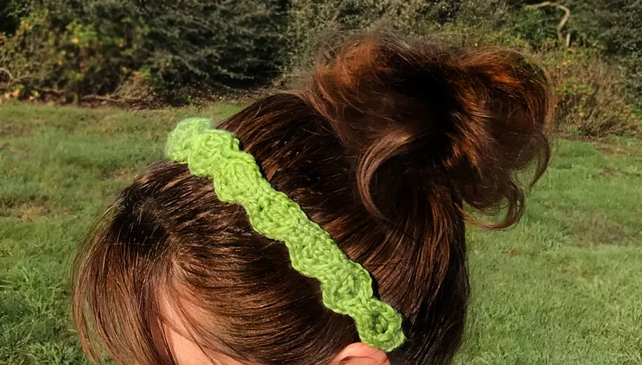 A close-up of a woman\'s head wearing a knitted headband in the honeycomb cable stitch pattern