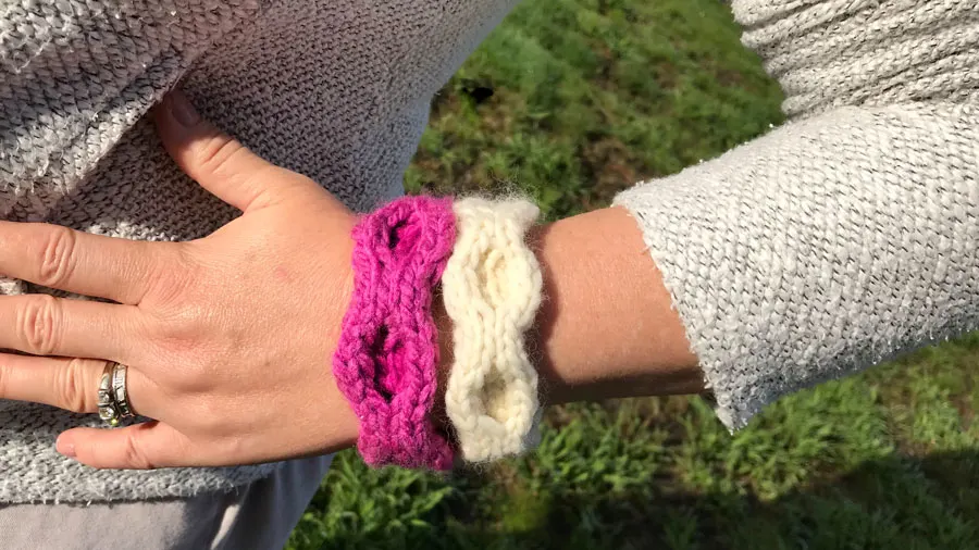 A close-up of an arm with two knitted honeycomb stitch bracelets in white and pink yarn
