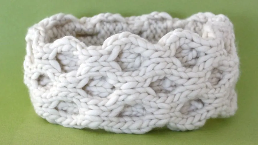 A close up of a knitted ear warmer in white yarn in the honeycomb cable stitch
