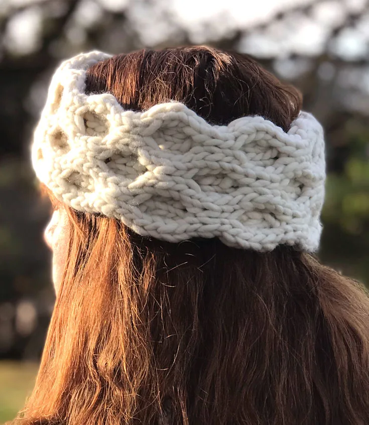 A close up of a woman\'s head wearing a knitted ear warmer in the honeycomb cable pattern stitch