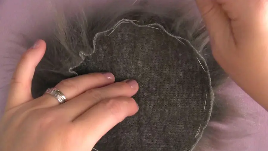 A close up of a hand cinching faux fur to make a pom pom.