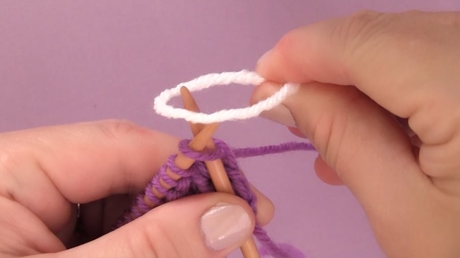 A white strand of yarn being added to straight knitting needles by a woman\'s hands.