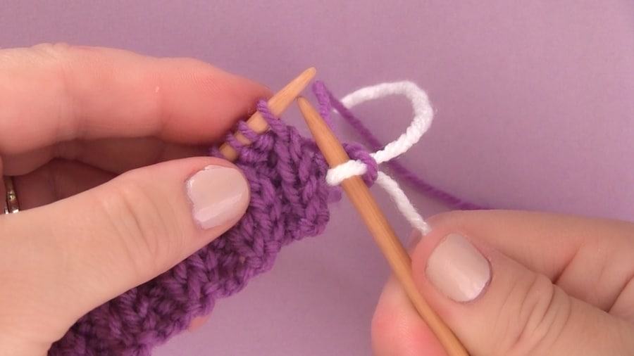 Two straight knitting needles held by a woman\'s hands with purple and white yarn.