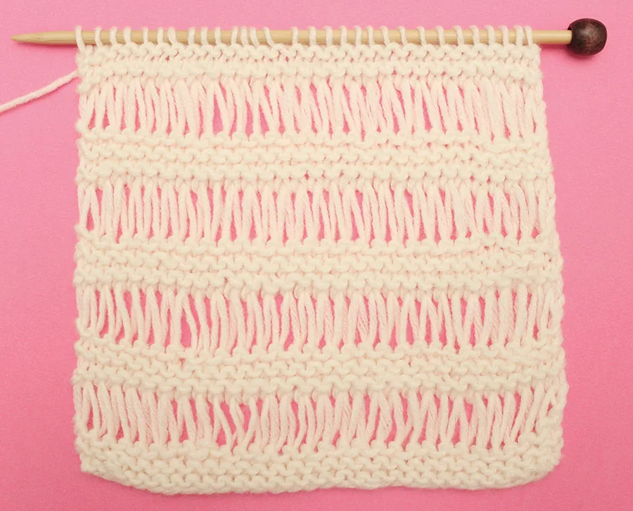Swatch of drop stitch knitting pattern with white yarn with stitches on a needle.
