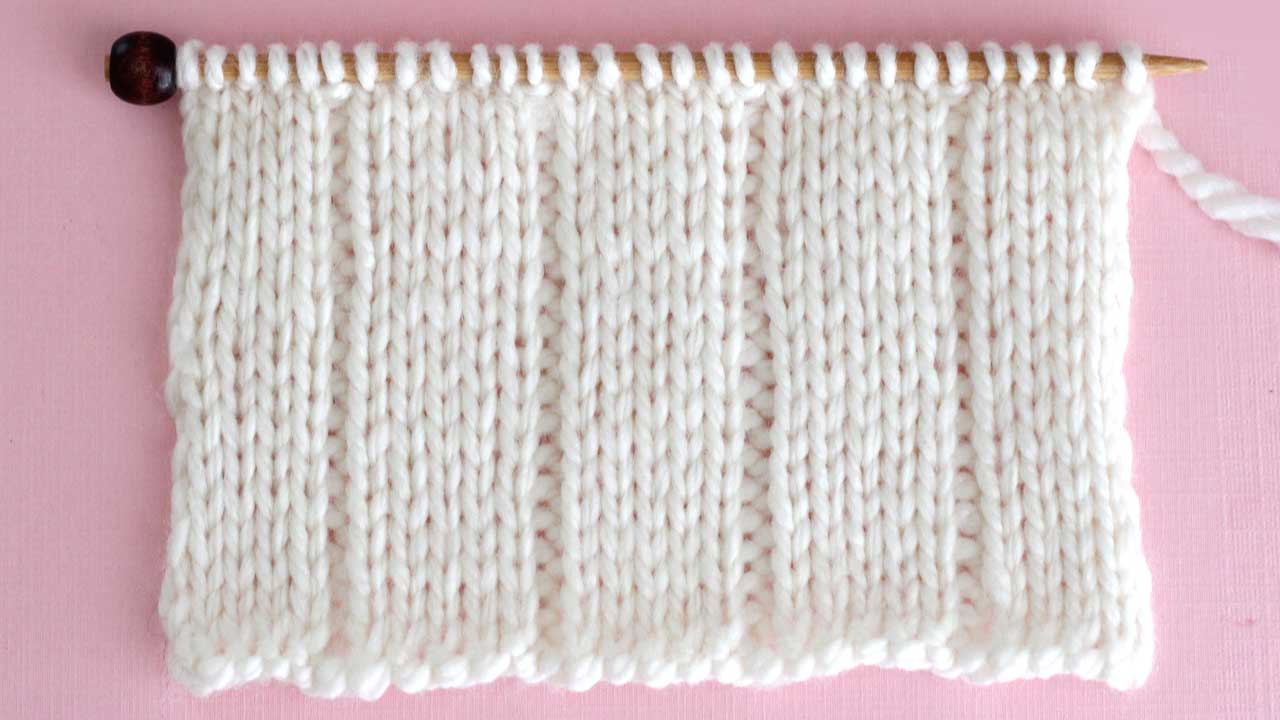 Close up a swatch of textured 5x1 Rib Stitch in white yarn on a knitting needle