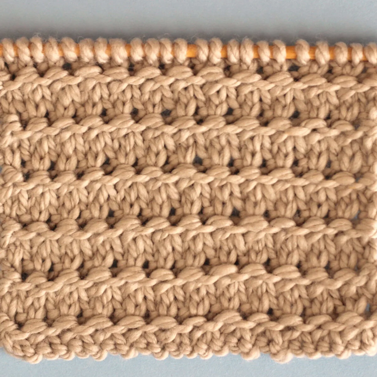 Knitting Swatch in the Granite Stitch Pattern texture in light brown yarn on a wooden bamboo knitting needle.