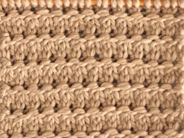 Knitting Swatch in the Granite Stitch Pattern texture in light brown yarn on a wooden bamboo knitting needle.