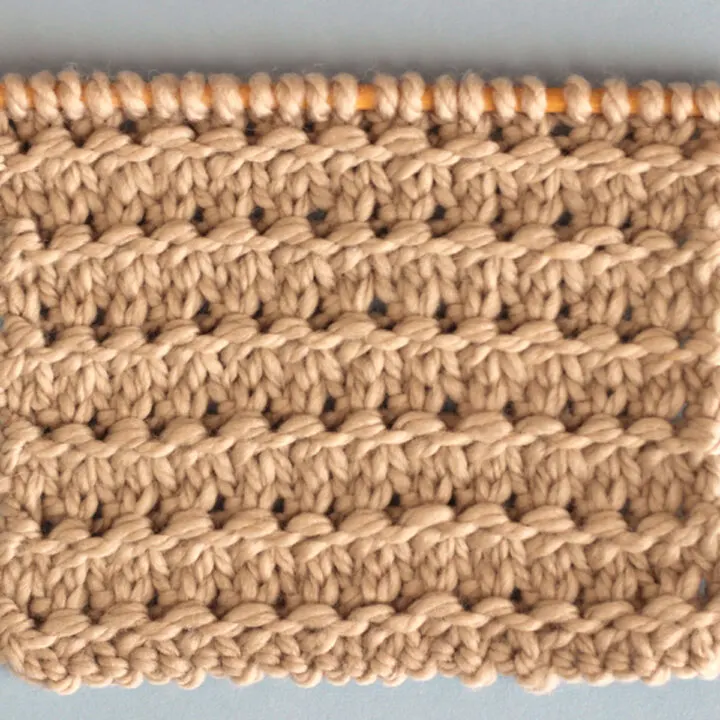 Knitting Swatch in the Granite Stitch Pattern texture in light brown yarn on a wooden bamboo knitting needle.