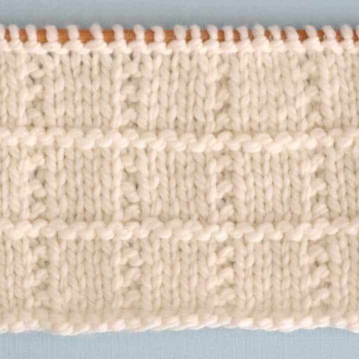 A close up of Tile Square knitted swatch in white yarn on straight knitting needle