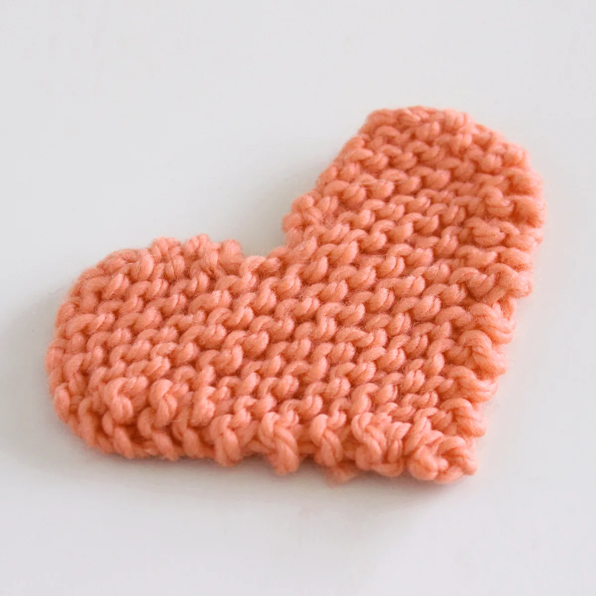 Knitted heart shape in garter stitch with orange color yarn.
