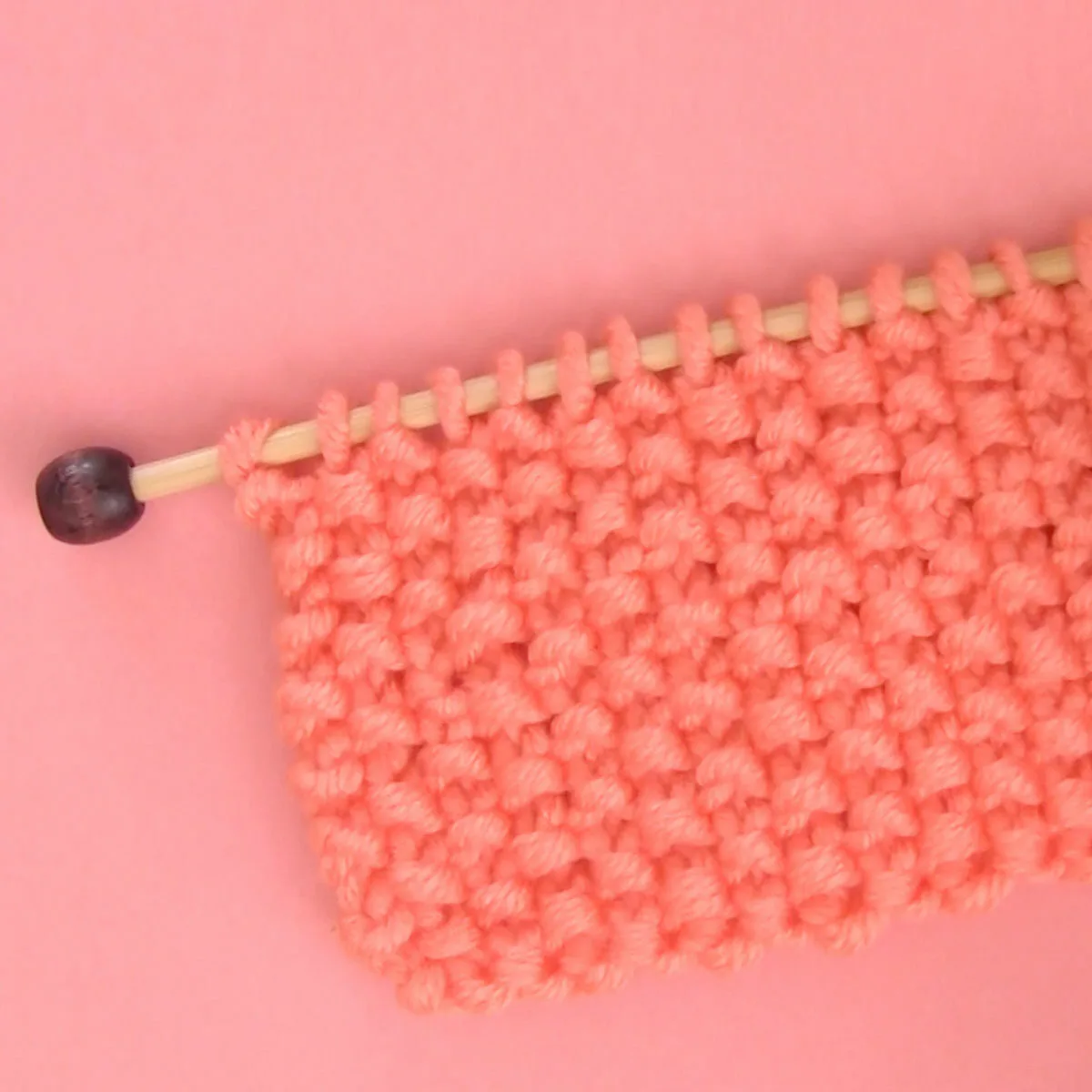 Seed Stitch Knitting swatch on a knitting needle in orange yarn.