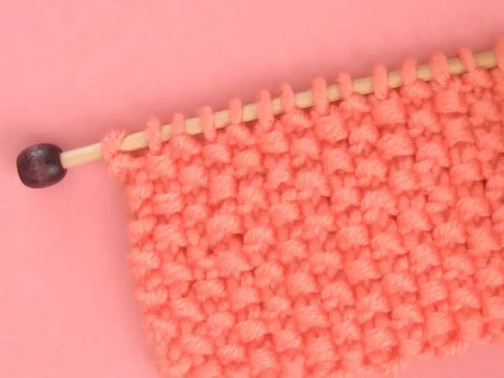 Seed Stitch Knitting swatch on a knitting needle in orange yarn.