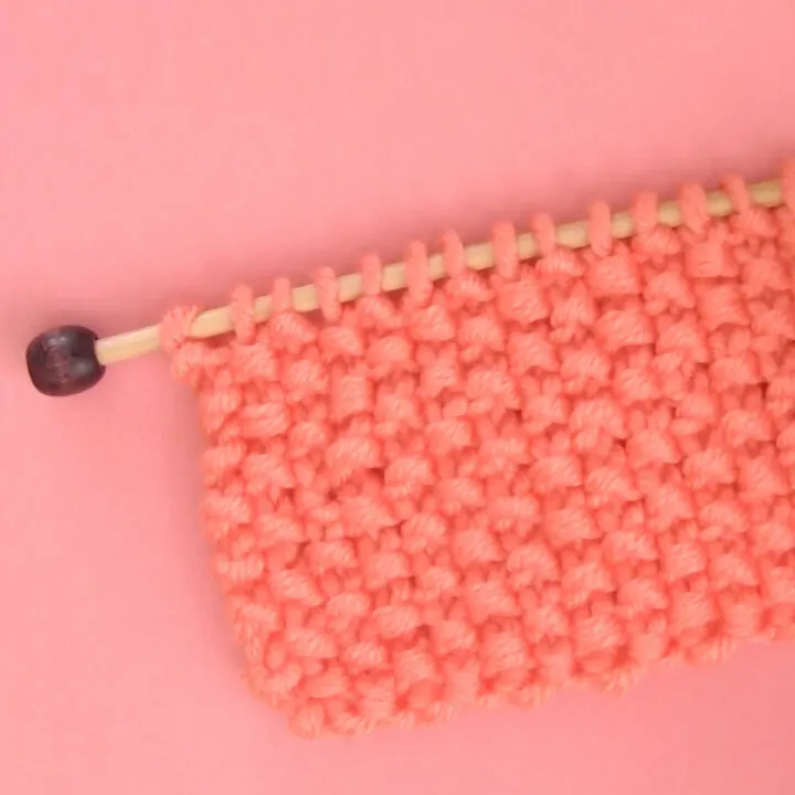 Seed Stitch Knitting swatch on a knitting needle in orange yarn.